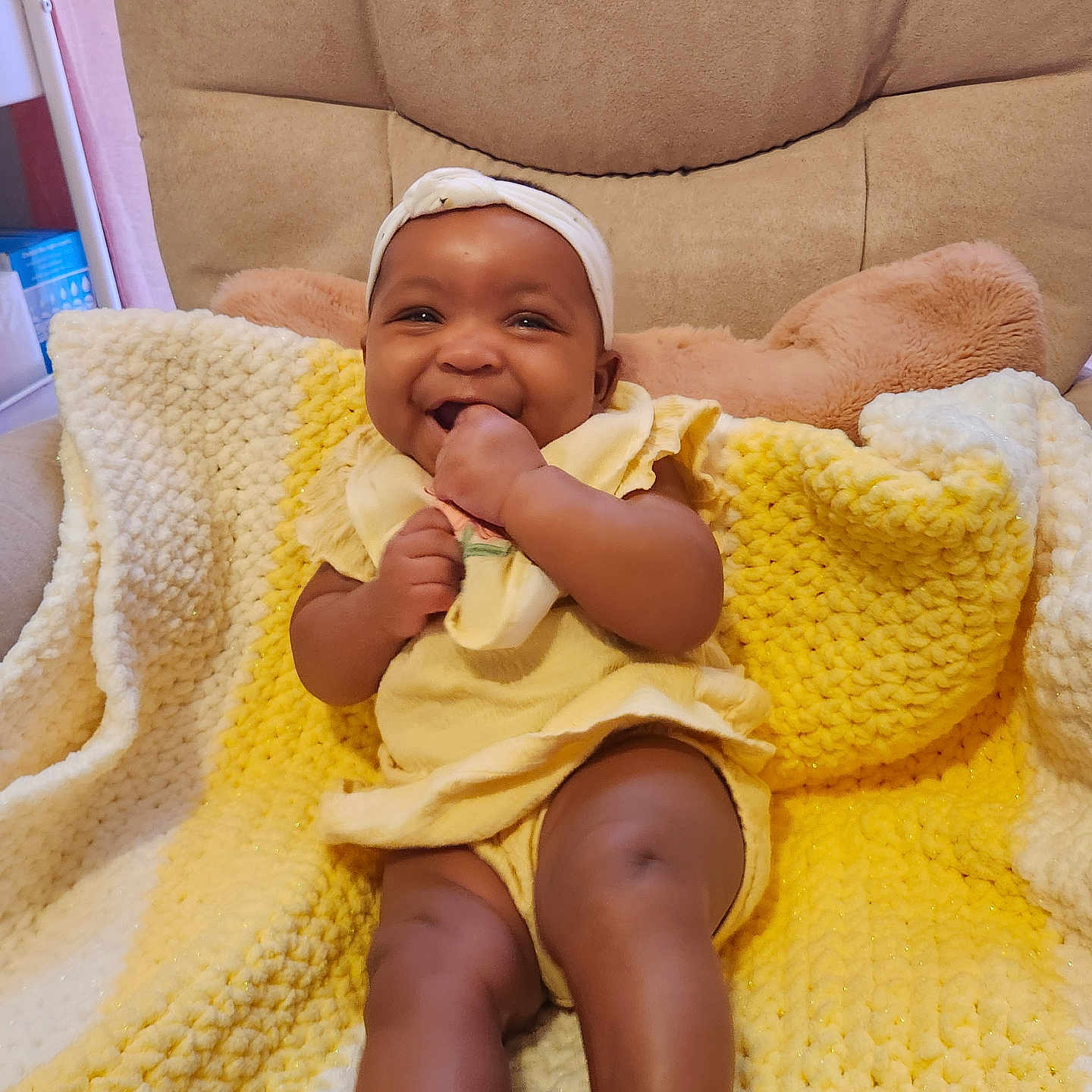 Naomi is registered to the contest to win money with this photo: baby, smiling, yellow_clothing, blanket, knit_blanket, infant, cute, happy, sitting, headband, hand, furniture, cushion, indoors, portrait, child, cozy, warm_colors, playful, young_child