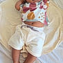 baby, infant, child, lying_down, blanket, bed, shorts, tshirt, patterned_clothing, barefoot, relaxed, cute, skin, face, legs, feet, one_arm_up, soft_fabric, indoors, comfort