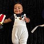 baby, smiling, child, infant, black_shirt, white_overalls, toy, lying_down, happy, cute, indoor, blanket, floor, wooden_floor, hand, face, person, portrait, clothing, cozy