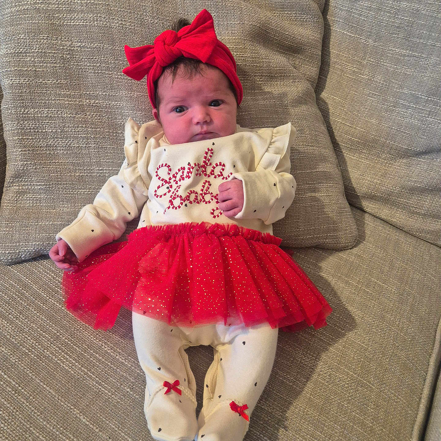 Isla-Rose joined the competition — help win amazing prizes! adorable, baby, child, couch, cushion, cute, fabric_texture, festive_clothing, footed_pajamas, headband, holiday_outfit, home_interior, indoor, infant, portrait, red_bow, red_tutu, resting, small_hands, white_onesie