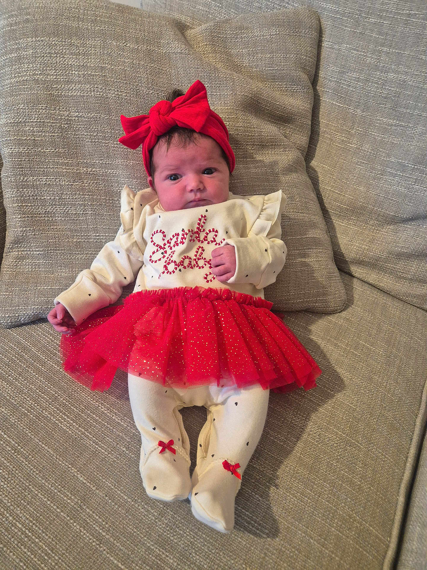 Isla-Rose joined the competition — help win amazing prizes! baby, infant, red_bow, red_tutu, festive_clothing, couch, cushion, white_onesie, footed_pajamas, home_interior, portrait, child, cute, holiday_outfit, indoor, fabric_texture, resting, adorable, small_hands, headband