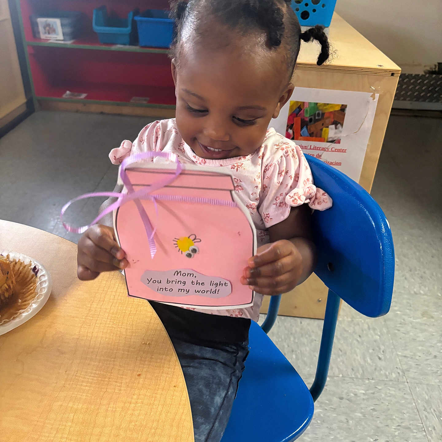 Jhazire joined the competition — help win amazing prizes! baskets, bee_drawing, blue_chair, child, classroom, clothing, craft, floor, hair, handmade_card, happy, indoor, muffin, person, pink, plate, shelves, smiling, table, toddler