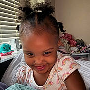 Jhazire joined the competition — help win amazing prizes! child, girl, smile, pigtails, rainbow_shirt, bed, blanket, toy, stuffed_animal, window_blinds, indoors, face, happy, cute, person, hair, playful, cozy, room, expression