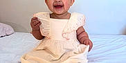 Aleia joined the competition — help win amazing prizes! baby, child, smiling, dress, sitting, barefoot, bed, white_bedspread, indoor, happy, infant, person, cute, portrait, young_child, chubby_cheeks, short_hair, light_background, furniture, home