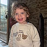 toddler, child, curly_hair, blue_eyes, smiling, sweatshirt, animal_print, indoor, stone_wall, door, sunlight, happy, portrait, person, casual_clothing, home, cozy, cute, young_child, fashion