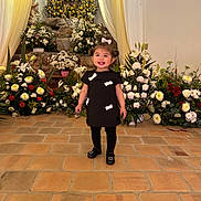 Delilah joined the competition — help win amazing prizes! altar, babyface, black_dress, ceremony, child, drapery, dress, event, floral_arrangement, flowers, girl, hair_bow, happy, indoor, portrait, shoes, smile, standing, tile_floor, toddler