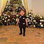altar, babyface, black_dress, ceremony, child, drapery, dress, event, floral_arrangement, flowers, girl, hair_bow, happy, indoor, portrait, shoes, smile, standing, tile_floor, toddler