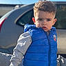 Leeroy participe au concours pour gagner de l'argent avec cette photo : child, toddler, boy, blue_vest, curly_hair, gray_sweatshirt, outdoor, car, sunlight, serious_expression, portrait, casual, young_child, person, clothing, daylight, standing, curious, background_blur, hands