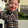 child, toddler, smiling, plaid_shirt, outdoor, sunlight, cup, happy, face, short_hair, person, daylight, joy, casual_clothing, young_child, cheerful, portrait, candid, emotion, expression