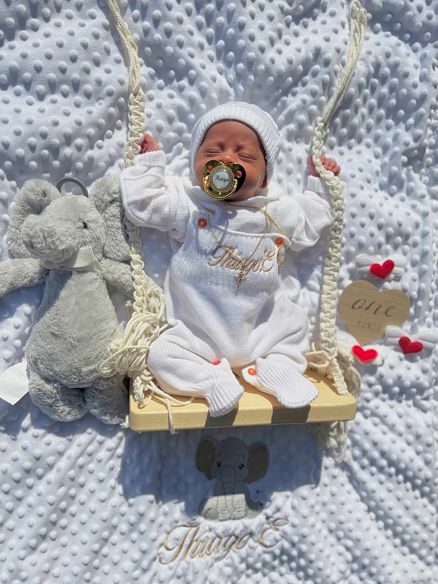 Thiago joined the competition — help win amazing prizes! baby, infant, swing, white_clothing, knit_hat, pacifier, plush_toy, elephant_toy, blanket, embroidery, wooden_swing, heart_decorations, one_month, sleeping, cute, soft_texture, rope, newborn, portrait, indoor