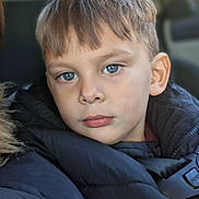 Eli is registered to the contest to win money with this photo: child, boy, blue_eyes, portrait, closeup, puffy_jacket, car_interior, seatbelt, warm_clothing, hair, face, expressionless, young, casual, indoors, natural_light, winter_wear, person, head_and_shoulders, sitting