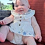 baby, child, smile, dress, headband, flower_pattern, white_clothing, outdoor, cushion, chair, happy, person, infant, cute, skin, legs, hand, seat, sunlight, portrait