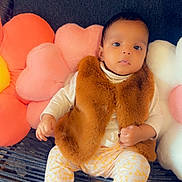 Milena participe au concours pour gagner de l'argent avec cette photo : baby, child, couch, pillow, flower_pillow, fur_vest, patterned_pants, soft_shoes, indoors, infant, cute, portrait, looking_at_camera, seated, comfortable, colorful, plush, cozy, small_hands, curious