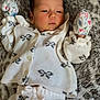 baby, infant, newborn, clothing, mittens, blanket, pattern, face, lying_down, soft_texture, cute, sleepwear, comfort, portrait, young_child, resting, white, floral, cozy, indoor