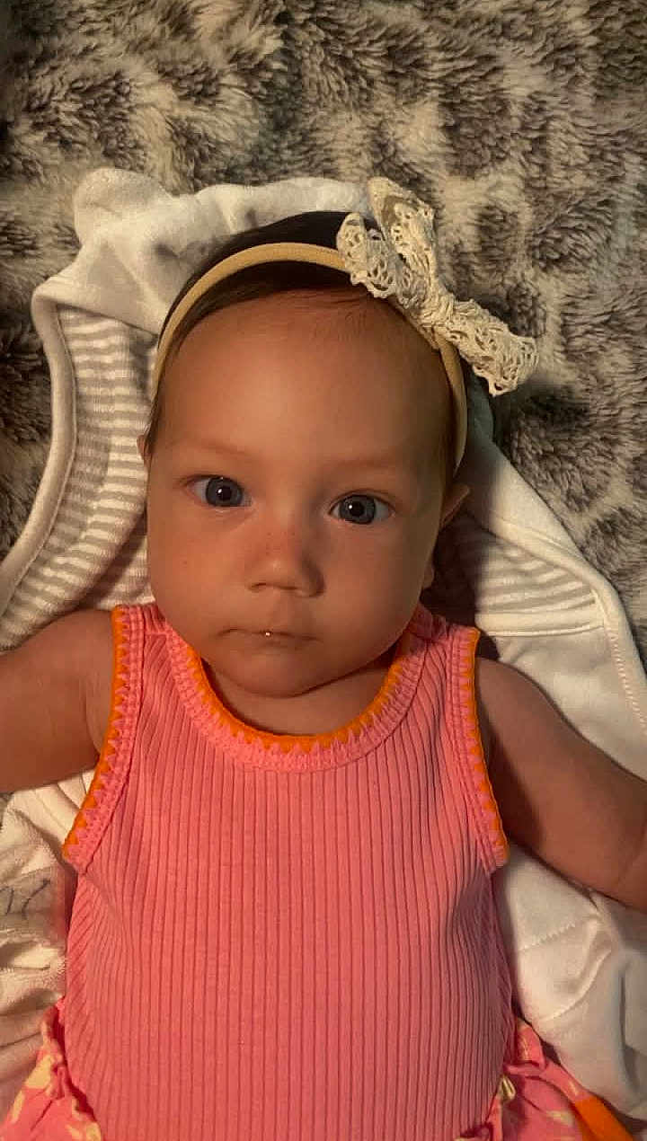 Willow is registered to the contest to win money with this photo: baby, child, face, headband, pink_clothing, blanket, portrait, infant, closeup, cute, expression, eyes, person, soft_texture, striped_blanket, indoor, laying_down, head, small_person, adorable