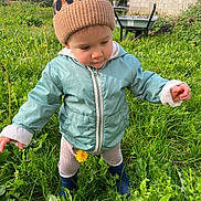 Alix participe au concours pour gagner de l'argent avec cette photo : toddler, child, beanie, jacket, grass, dandelion, boots, outdoor, garden, nature, greenery, wall, wheelbarrow, daylight, curious, standing, exploring, plants, cold_weather, casual_clothing