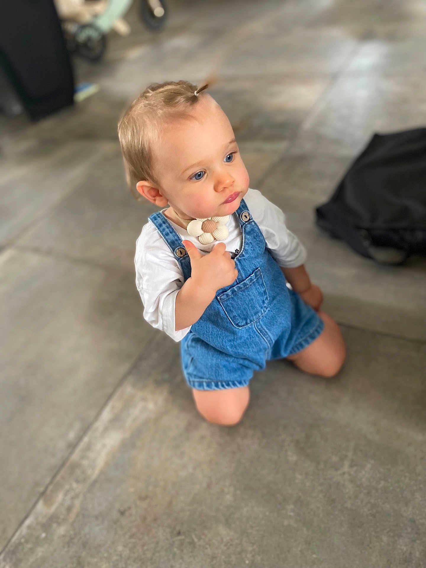 Alix participe au concours pour gagner de l'argent avec cette photo : toddler, child, denim_overalls, white_shirt, kneeling, indoor, concrete_floor, blue_eyes, ponytail, curious, casual_clothing, small_hands, cute, young_child, portrait, person, baby, innocent, looking_away, floor
