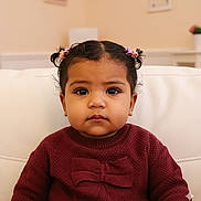 Avalyn is registered to the contest to win money with this photo: bow, child, couch, cozy, cute, earrings, expression, face, girl, hair_ties, home_interior, indoor, maroon_sweater, pigtails, portrait, seated, toddler, warm_lighting, white_couch, young_child