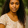 young_girl, portrait, curly_hair, floral_top, outdoor, nature_background, female, person, face, eyebrows, eyes, skin, shoulders, casual_clothing, earrings, natural_light, calm_expression, standing, youth, closeup