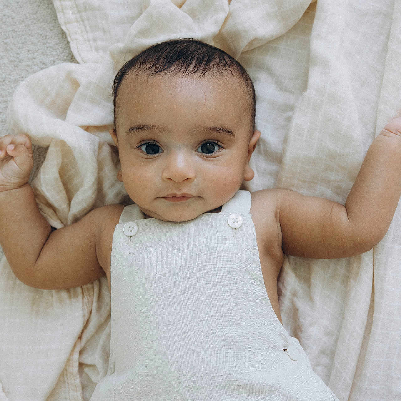 Yugveer Reddy is registered to the contest to win money with this photo: baby, infant, child, blanket, soft, cute, portrait, lying_down, clothing, white_outfit, arms_outstretched, indoors, skin, face, head, eyes, hands, expression, young, adorable