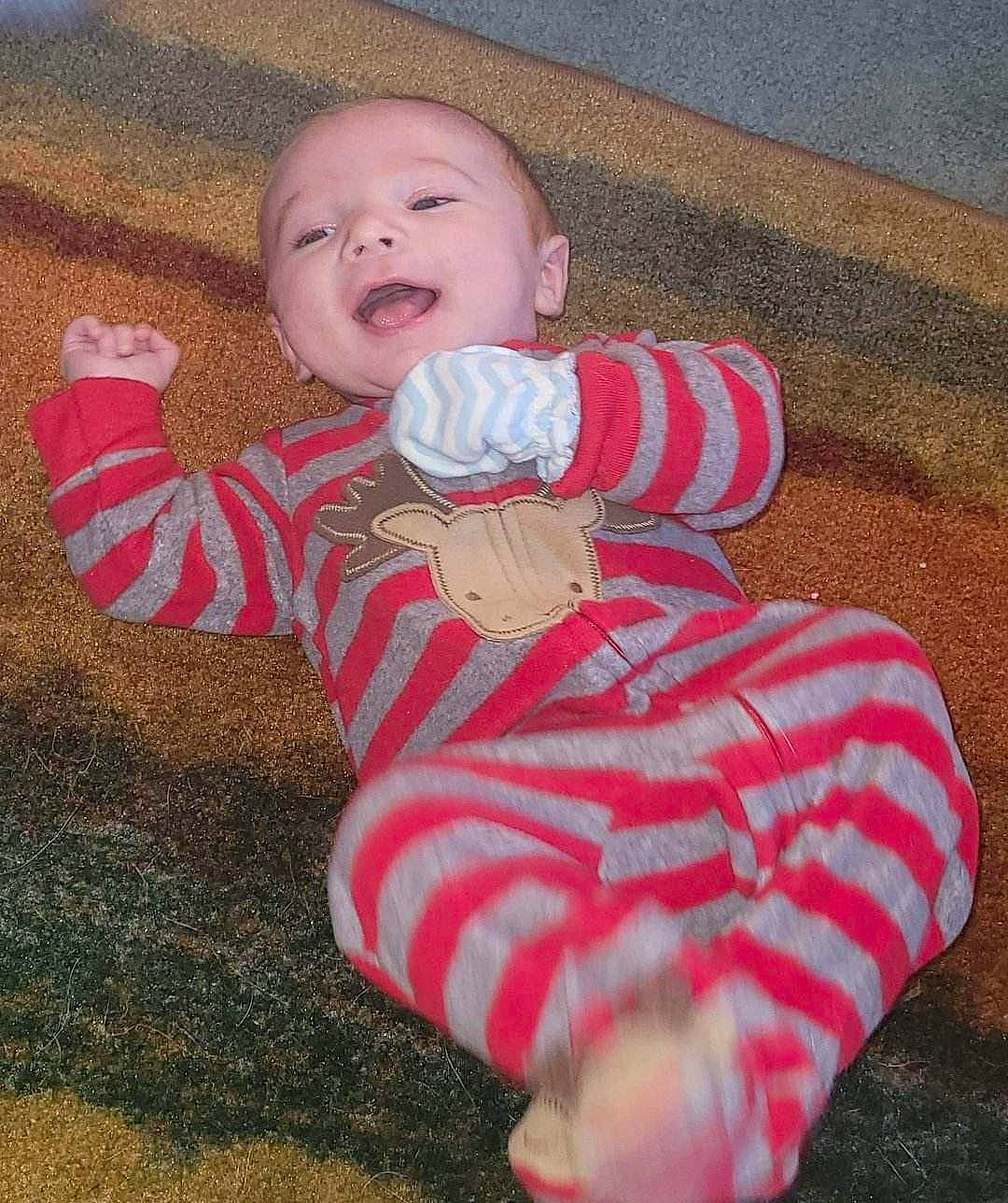 Jude is registered to the contest to win money with this photo: arm, baby, baby_laughing, baby_toddler_clothing, cheek, comfort, eye, face, finger, flooring, grass, happy, head, nose, person, pink, skin, sleeve, smile, thumb