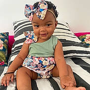 Kalycia a rejoint le concours — aidez-le/la à gagner de superbes lots ! baby, child, smile, bow, headband, curly_hair, striped_bedding, floral_pattern, hand, foot, sitting, indoors, pillow, cute, infant, happy, skin, person, one_person, portrait