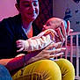 Celeste participe au concours pour gagner de l'argent avec cette photo : affection, baby, baby_clothing, bond, cradle, crib, curiosity, dark_clothing, face, gentle, human_hand, indoor, parent_and_child, room, seated, smile, soft_lighting, wall_decor, woman, yellow_pants