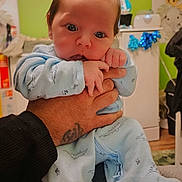 Ezekiel is registered to the contest to win money with this photo: baby, infant, child, portrait, indoors, nursery, held, hands, smiling, calm, blue_outfit, onesie, baby_clothing, animal_pattern, green_wall, stuffed_animals, home, family, closeup, photography