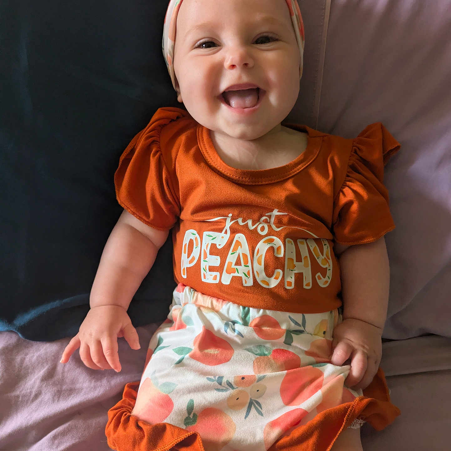Lainey joined the competition — help win amazing prizes! apparel, baby, bed, child, comfort, cute, expression, face, happy, headband, human, indoors, infant, orange_clothing, person, pillow, portrait, sitting, skin, smiling