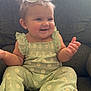 baby, child, smiling, sitting, indoors, couch, green_clothing, daisy_pattern, sunglasses, hair_pigtails, happy, cute, portrait, furniture, barefoot, infant, home, casual, playful, comfortable