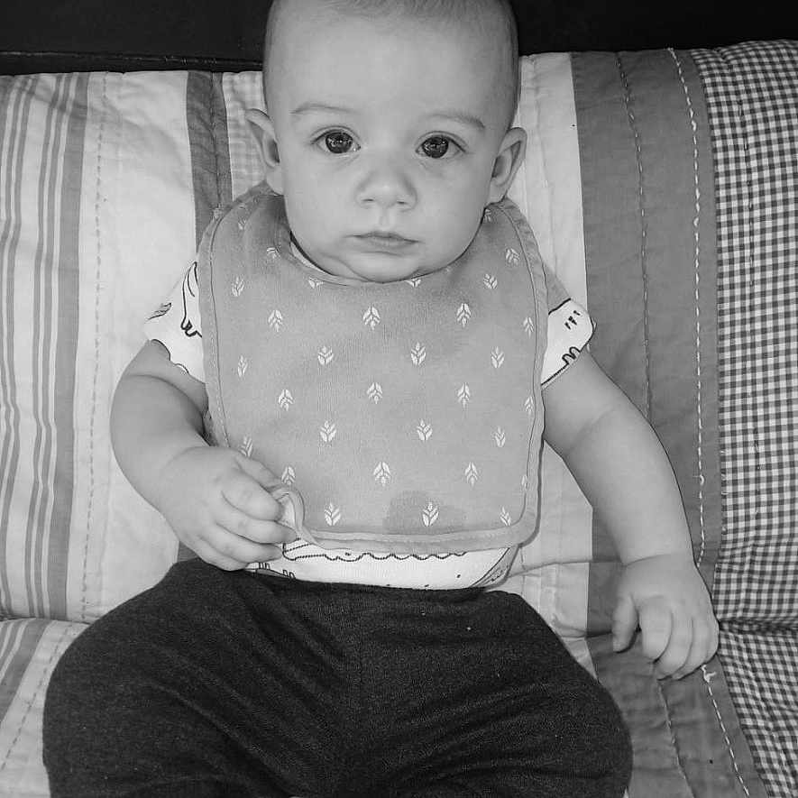 Rowdie joined the competition — help win amazing prizes! baby, bib, black_and_white, child, clothing, cute, expression, eyes, face, hand, head, indoors, infant, pants, pattern, person, portrait, quilt, sitting, young