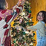 Estrella joined the competition — help win amazing prizes! adult, celebration, child, christmas_tree, curly_hair, decorating, family, festive, happy, holiday, indoor, joy, lights, ornaments, overalls, seasonal, smile, sweater, togetherness, wood_paneling