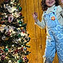 Estrella joined the competition — help win amazing prizes! blue_overalls, celebration, child, christmas_tree, curly_hair, dancing, decorations, family, festive, flower_decoration, happy, holiday, indoor, joyful, lights, ornaments, person, pine_cones, smiling, wood_panel_wall