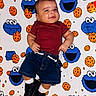Eleggúasdiel joined the competition — help win amazing prizes! baby, black_shoes, blanket, casual_clothing, child, colorful, cookie_monster, cookie_pattern, cute, denim_shorts, happy, indoors, infant, lying_down, maroon_shirt, patterned_background, playful, portrait, smiling, white_socks