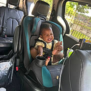 Yemi joined the competition — help win amazing prizes! baby, infant, child, car, car_seat, laughing, smiling, happiness, portrait, indoor, vehicle, safety_harness, seatbelt, toes, bare_feet, yellow_shirt, teal, leather_seats, sunlight, trees