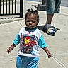 Yemi is registered to the contest to win money with this photo: child, toddler, boy, outdoor, sidewalk, street, portrait, standing, walking, iron_man, superhero, marvel, t_shirt, shorts, sneakers, adult, sunlight, fence, urban, shadow