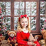 child, girl, red_dress, headband, bow, teddy_bear, plush_toy, christmas_tree, ornament, gift_box, window, snow, holiday, festive, smile, indoors, decoration, celebration, winter, happy