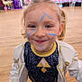 child, face_paint, smiling, indoor, party, costume, blonde_hair, curly_hair, blue_eyes, wooden_floor, people, background, celebration, young, portrait, happy, clothing, jacket, event, fun