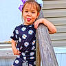 casual, child, cute, daisy_print, daylight, expression, fun, girl, hair_tied, matching_outfit, outdoor, person, playful, purple_bows, smile, standing, summer_clothing, tongue_out, wooden_railing, young