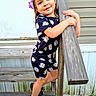 casual, child, daisy, daylight, flower_pattern, girl, grass, happy, nature, outdoor, person, playful, portrait, purple_bow, sandals, smile, standing, summer_clothing, wood, wooden_railing