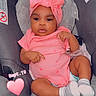 baby, infant, child, portrait, car_seat, pink_outfit, headband, bow, hearts, socks, seated, indoors, vehicle, sleeping_baby_seat, looking_at_camera, dark_skin, cute, date_text, heart_sticker, baby_fashion