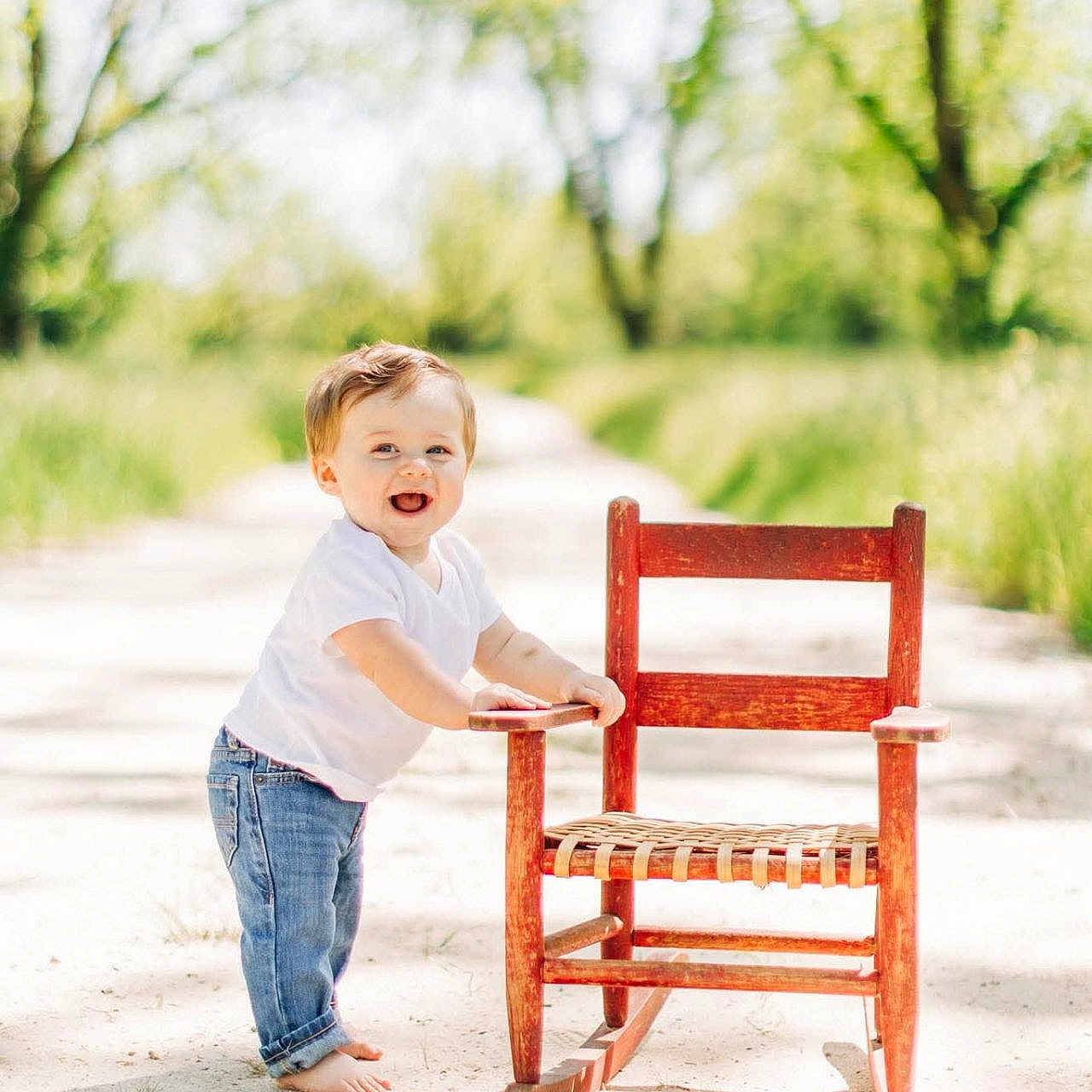 Turner joined the competition — help win amazing prizes! toddler, child, rocking_chair, barefoot, smiling, outdoor, path, trees, greenery, sunlight, jeans, white_shirt, happy, nature, daylight, portrait, playing, young_child, casual, summer
