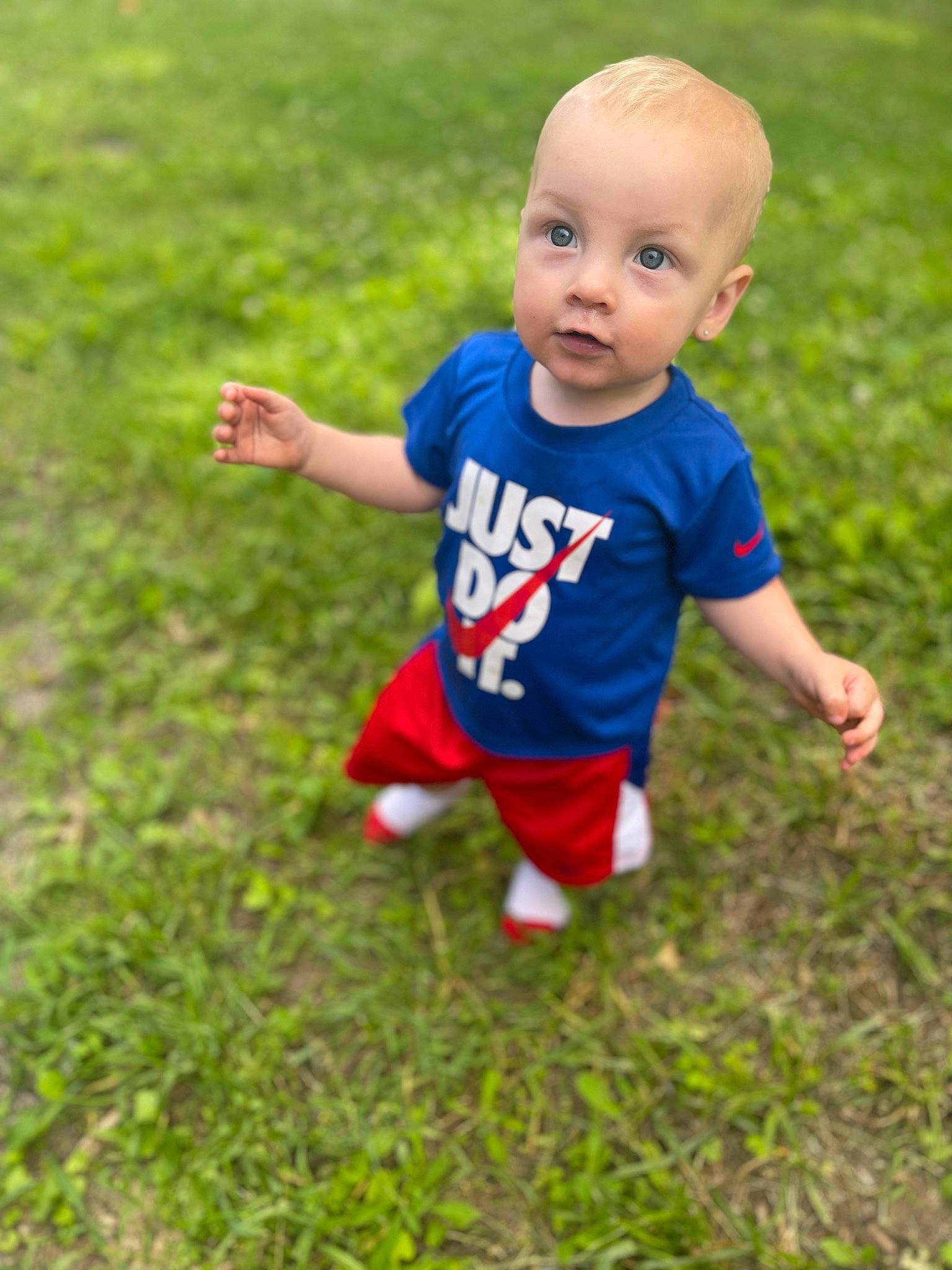 Julian is registered to the contest to win money with this photo: baby, baby_toddler_clothing, clothing, finger, flooring, gesture, grass, grassland, hand, happy, leg, meadow, people_in_nature, person, plant, recreation, shoe, sleeve, smile, t_shirt