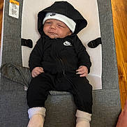 Kamarion is registered to the contest to win money with this photo: baby, infant, nike, hoodie, hat, socks, baby_rocker, gray, white, black_clothing, indoor, footwear, cute, child, resting, portrait, smile, person, apparel, relaxing