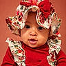 adorable, baby, background, bow, child, closeup, cute, expression, eyes, face, fashion, floral, hat, headwear, infant, portrait, red_clothing, smile, warm_colors, young