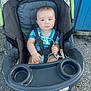 baby, child, stroller, pacifier, outdoor, blue_wall, gravel, seat, harness, infant, person, clothing, toy, hand, face, expression, hair, sitting, cute, safety