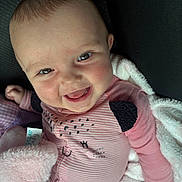 Aphelia Kay is registered to the contest to win money with this photo: baby, smiling, face, pink_clothing, blanket, soft_texture, happy, infant, cute, portrait, child, closeup, cozy, sitting, indoors, skin, eyes, mouth, hand, furniture