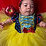 baby, child, face, costume, snow_white, yellow_tutu, red_bow, apple, portrait, cute, infant, fabric, dress, headband, red_background, curious, closeup, indoor, soft_lighting, person