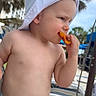 Lucas is registered to the contest to win money with this photo: toddler, child, baby, hat, diaper, snack, outdoor, palm_tree, sunny, summer, lounge_chair, eating, young_child, cute, person, vacation, nature, blue_sky, playful, fun