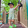 Lucas is registered to the contest to win money with this photo: toddler, child, playground, outdoor, green_shoes, cap, steering_wheel, clothing, person, play_equipment, trees, summer, daylight, cute, standing, fun, park, metal_platform, handrail, young_child